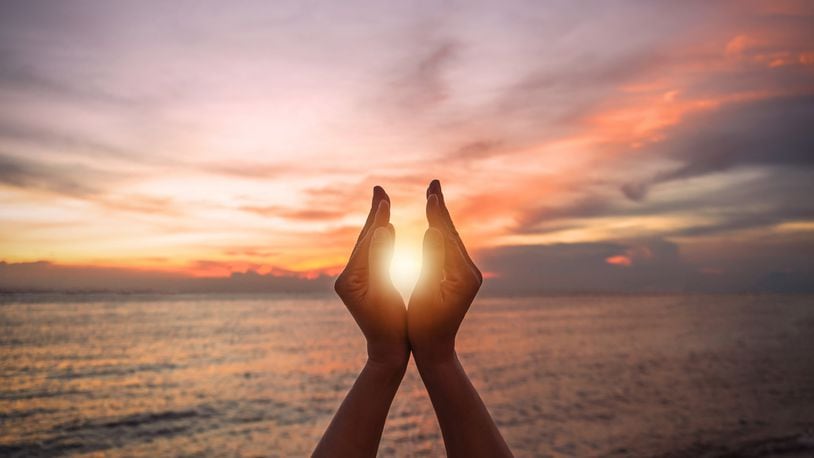 June summer sun solstice concept with silhouette of happy young woman's hands relaxing, meditating and holding sunset against warm golden hour sky. CHINNAPONG/ISTOCK