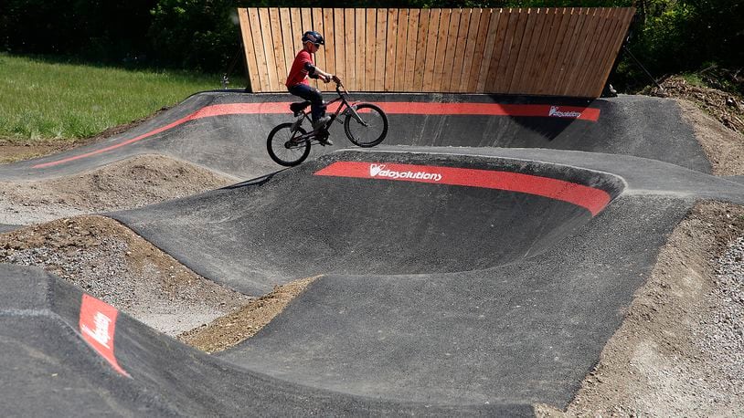 Miles Brehm, 8, tries out the new National Trail Parks and Recreation pump track at Sherman Park Monday, May 13, 2024. The pump track is an asphalt track for cycling. It has a circuit of hills, banked turns and features designed to be ridden completely by riders "pumping" - generating momentum by up and down body movements, instead of pedaling or pushing. BILL LACKEY/STAFF