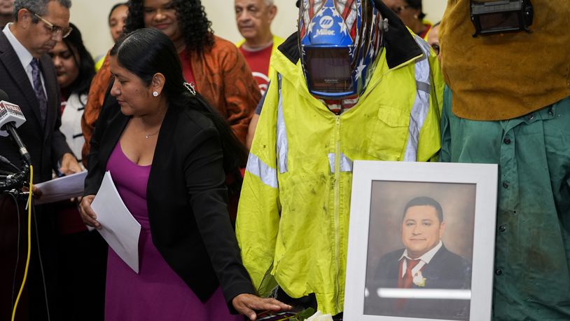 Maria del Carmen Castellón, the wife of Miguel Luna, a welder who died during the collapse of Baltimore's Francis Scott Key Bridge, places a rose near a portrait of her husband and his welding gear before speaking during a press conference, Tuesday, Sept. 17, 2024, in Baltimore. (AP Photo/Stephanie Scarbrough)