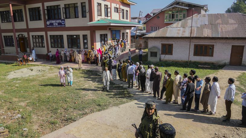 Indian paramilitary soldiers guard as Kashmiris queue up at a polling booth to cast their vote during the final phase of an election to choose a local government in Indian-controlled Kashmir, north of Srinagar, Tuesday, Oct.1, 2024. (AP Photo/Mukhtar Khan)