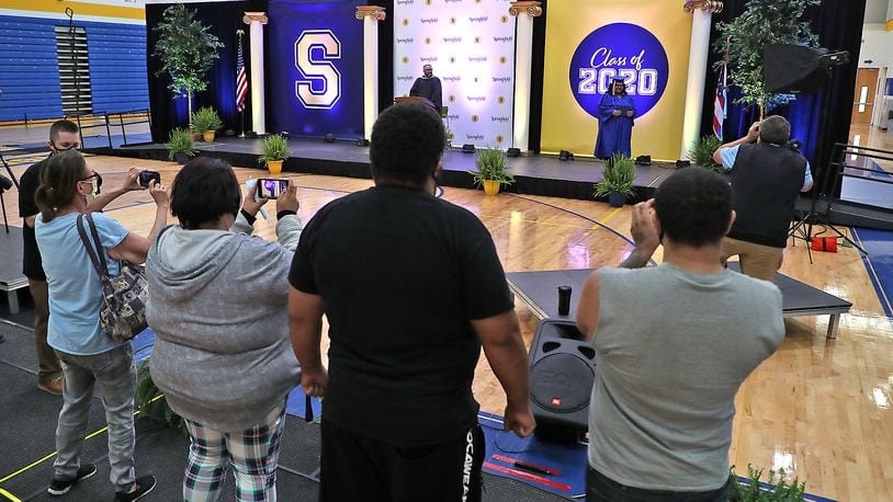 Clark and Champaign County schools will host their 2021 graduation ceremonies outside. Here, a family takes pictures of their Springfield High School graduate as she receives her diploma in an individual ceremony in 2020. BILL LACKEY/STAFF