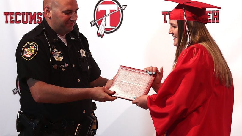 Deputy John Loney, school resource officer at Tecumseh Local Schools, presents Ellie Gehret with her diploma Monday during her individual graduation ceremony. BILL LACKEY/STAFF