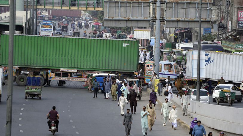 People try to cross through shipping containers set up by authorities to prevent supporters of imprisoned former Prime Minister Imran Khan from holding a rally to demand his release in Lahore, Pakistan, Saturday, Oct. 5, 2024. (AP Photo/K.M. Chaudary)