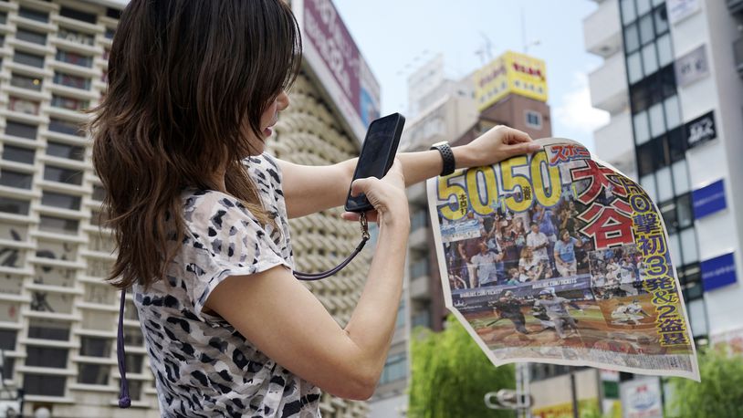 A pedestrian takes a photo of an extra edition of the Sports Nippon newspaper reporting on the Los Angeles Dodgers' Shohei Ohtani becoming the first player in major league history with 50 home runs and 50 stolen bases in a season, Friday, Sept. 20, 2024, in Tokyo. (AP Photo/Eugene Hoshiko)