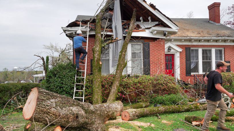 People work to clear a tree from a storm damaged home in Newnan, Ga., on Friday, March 26, 2021. Dozens of tornadoes tore across Alabama and Georgia beginning on Thursday, leaving at least six dead and many neighborhoods in tatters. (Johnathon Kelso/The New York Times)
