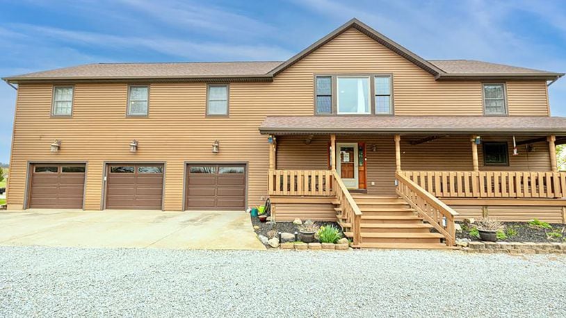 The front of the home features a covered wood front porch with railings and wood beams on the ceiling. The three car attached garage has extended area with a workshop.