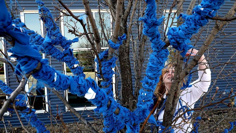 Kristi Limes wraps branches of a tree in front of the Hollenbeck-Bayley Conference Center with blue ribbons as she works on the Project Jericho Blue Ribbon Tree for Child Abuse Awareness Month. BILL LACKEY/STAFF