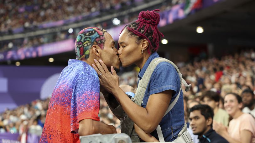 Roderick Townsend of the United States kisses his wife Tynita Townsend, with their son Rodney Townsend, between Rodrick's jumps in the T47 Men's High Jump at the 2024 Paralympics, Sunday, Sept. 1, 2024 in Paris, France. (AP Photo/Caleb Craig)