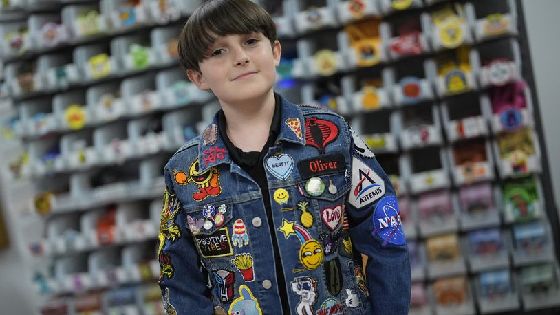 Oliver Burkhardt, 13, stands in front of trays of patches inside the offices of the Oliver Patch Project, Wednesday, Sept. 4, 2024, in Miami. (AP Photo/Rebecca Blackwell)