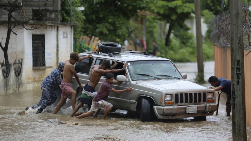 Residents work together to push a vehicle stuck on a street flooded by the passing of Hurricane John, in Acapulco, Mexico, Friday, Sept. 27, 2024. (AP Photo/Bernardino Hernandez)