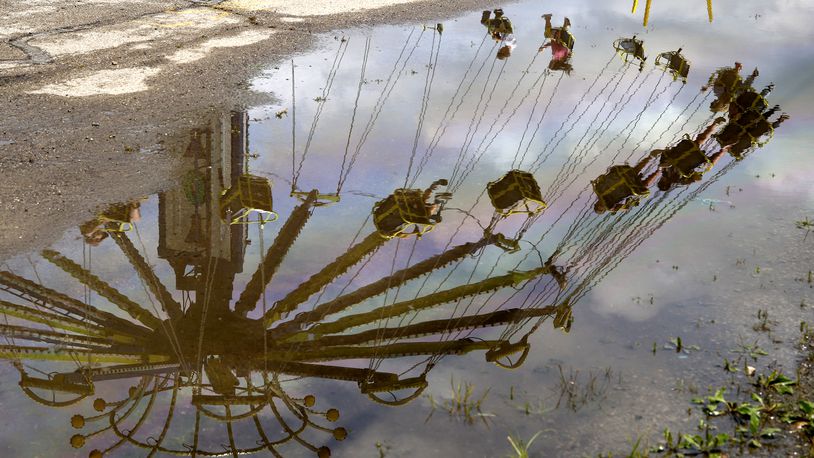 Riders of the YOYO swing ride on the midway at the Clark County Fair are reflected in a rain puddle Monday, July 22, 2024. BILL LACKEY/STAFF