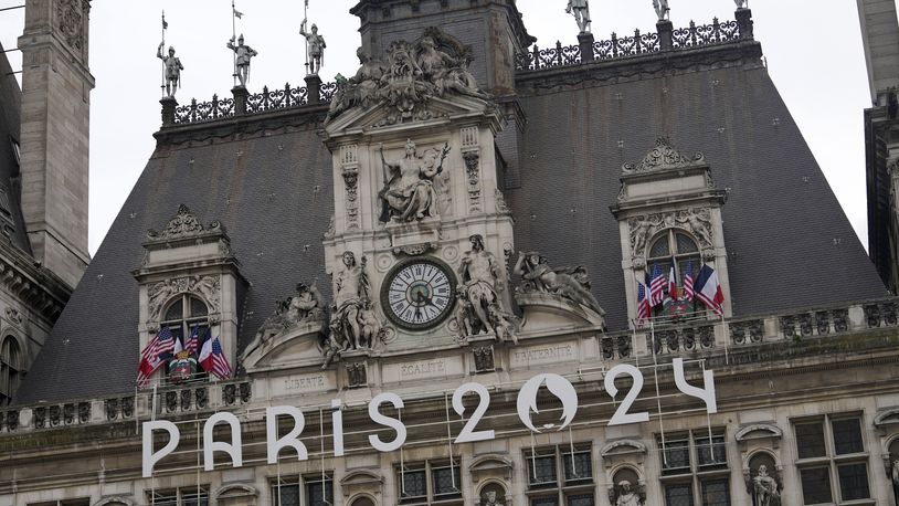 The logo of the Paris 2024 Olympic Games hangs from the facade of the Paris city hall, Wednesday, July 3, 2024 in Paris. Just three weeks before the Olympics, the excitement that was building up in the host city has mingled with anxiety about France’s political future. (AP Photo/Thibault Camus)