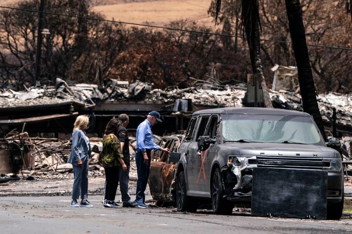 President Joe Biden touches a burnt car as he visits areas devastated by wildfires with first lady Jill Biden, left, Gov. Josh Green of Hawaii, and his wife, Jamie Green, in Lahaina, Hawaii, on Aug. 21, 2023. (Haiyun Jiang/The New York Times)