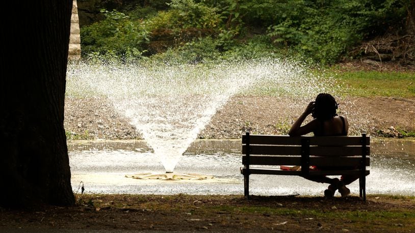 A woman finds relief from the heat on a park bench in the shade while she watches the fountain in the middle of the Snyder Park Lagoon. BILL LACKEY/STAFF