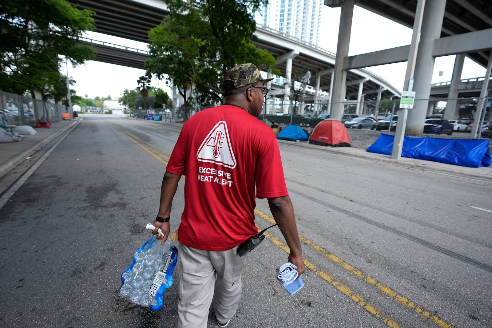 FILE - Ricky Leath, an outreach specialist with the City of Miami, walks through a homeless encampment as he works with the Miami-Dade County Homeless Trust to distribute bottles of water and other supplies to the homeless population, helping them manage high temperatures, May 15, 2024, in Miami. (AP Photo/Lynne Sladky, File)