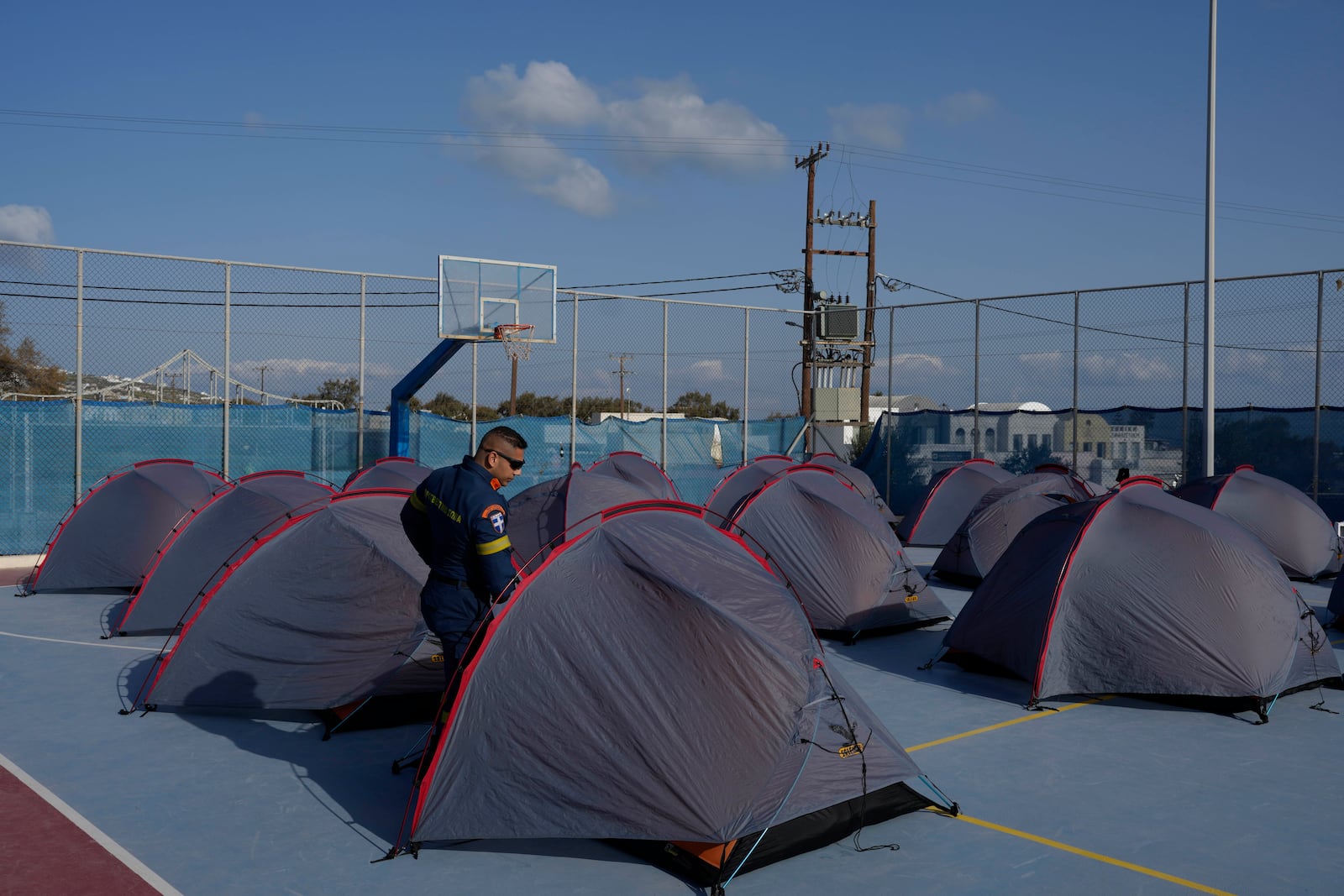 A firefighter walks among tents set up at a basketball court to accommodate Fire Service rescuers as Greek authorities are taking emergency measures in response to intense seismic activity on the popular Aegean Sea holiday island of Santorini, southern Greece, Monday, Feb. 3, 2025. (AP Photo/Petros Giannakouris)