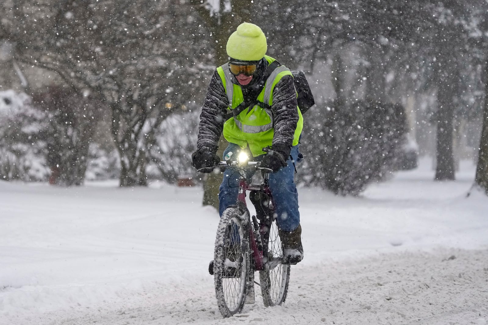 A biker makes their way on a street during a snowfall Wednesday, Feb. 12, 2025, in Shorewood, Wis. (AP Photo/Morry Gash)