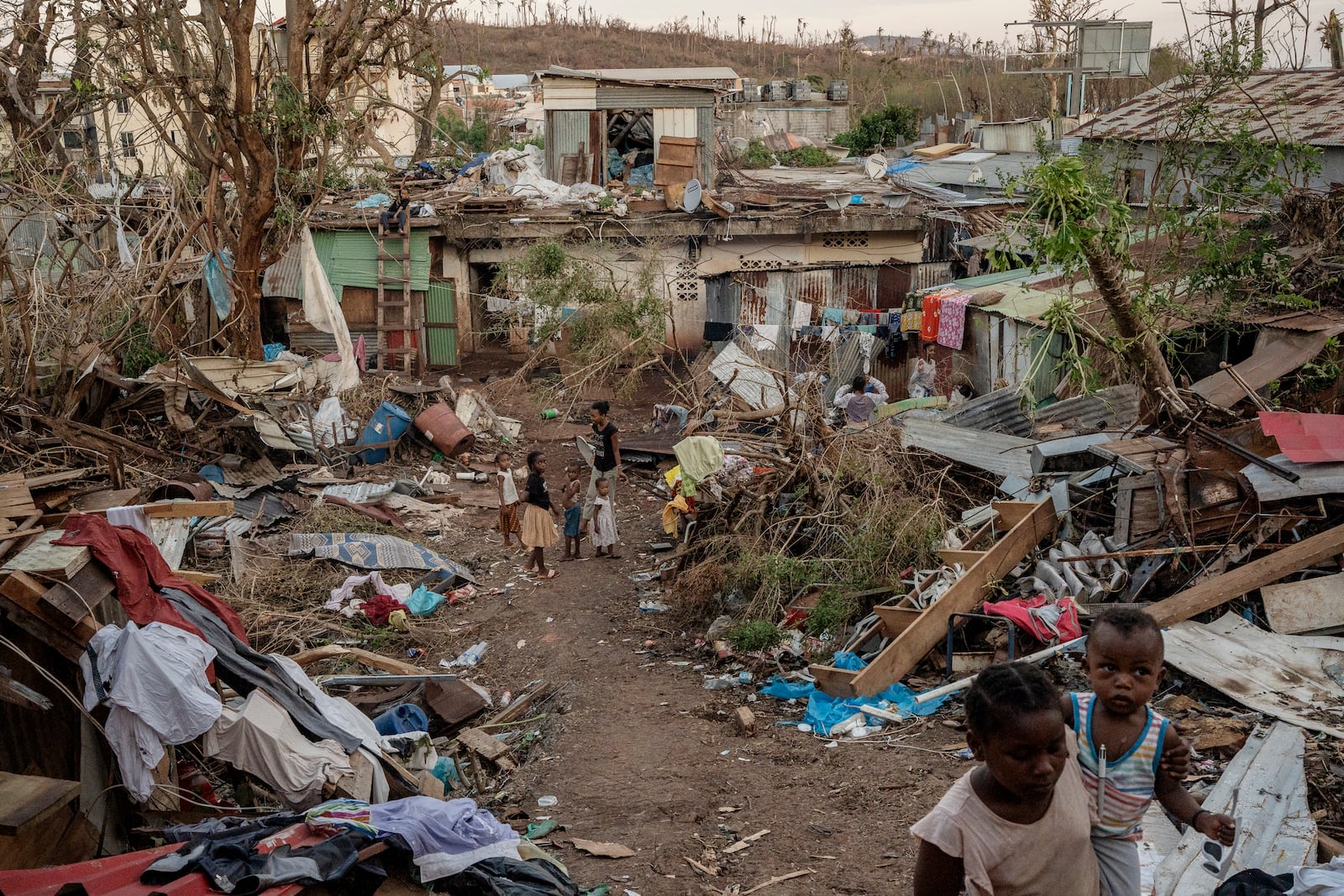 A family stands in the middle of wreaked houses in Mamoudzou, Mayotte, Thursday, Dec. 19, 2024 (AP Photo/Adrienne Surprenant)