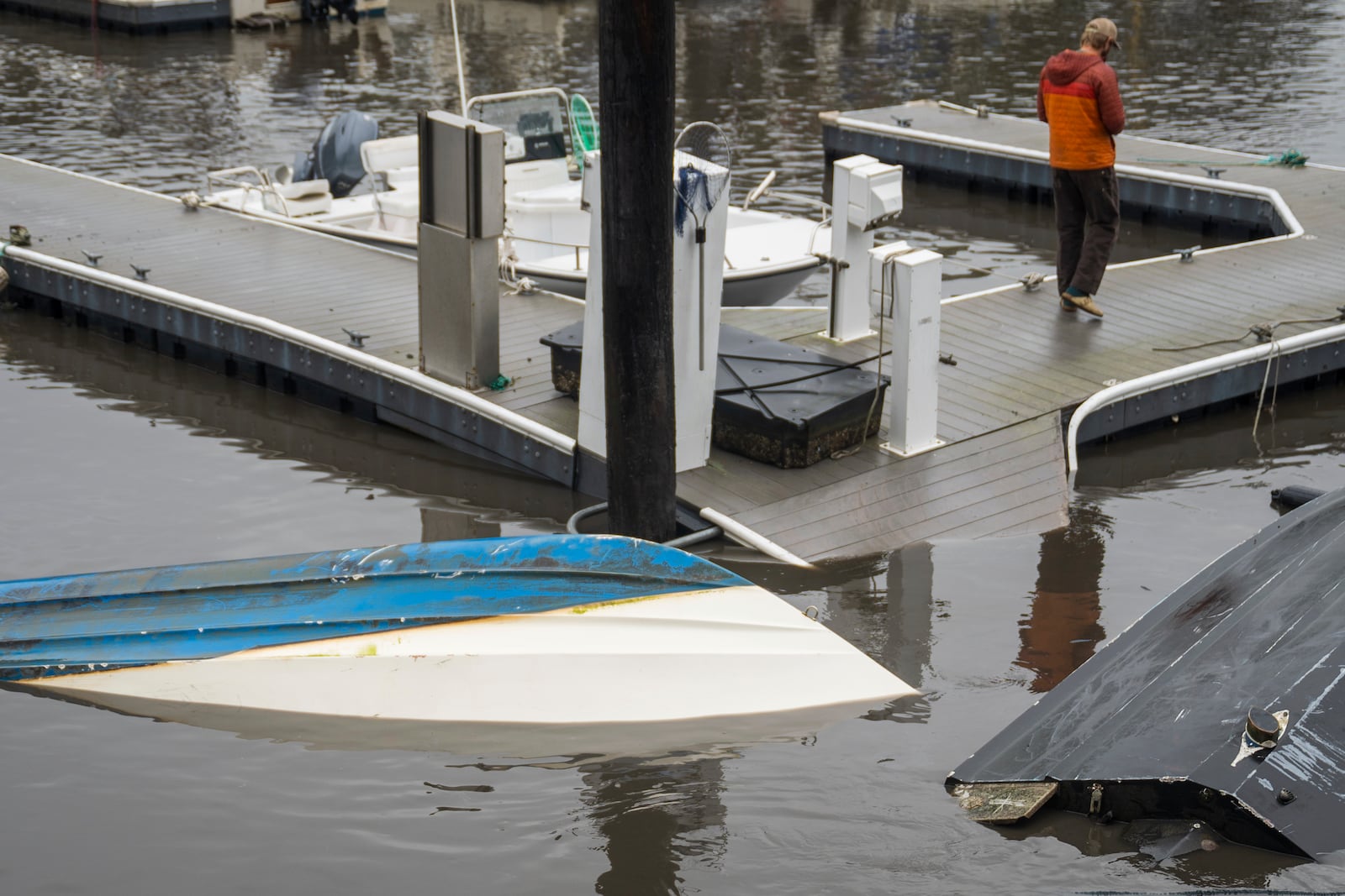 A man walks by overturned boats in Santa Cruz Harbor in Santa Cruz, Calif., Tuesday, Dec. 24, 2024. (AP Photo/Nic Coury)