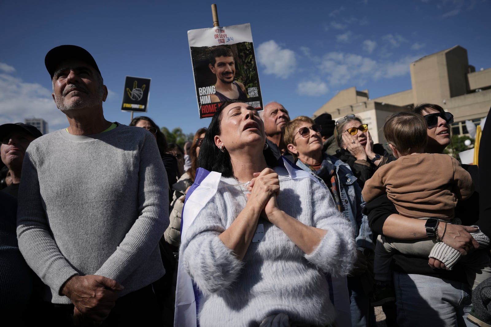 People holding posters with photos of Israelis hostages Eli Sharabi, Or Levy and Ohad Ben Ami, react at the so-called "hostages square" as they watch their release live on a television screen in Tel Aviv, Israel on Saturday, Feb. 8, 2025. (AP Photo/Oded Balilty)