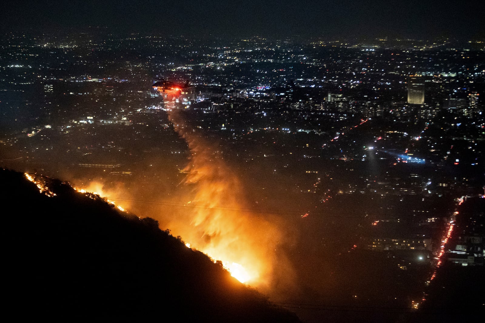 Water is dropped by helicopter on the burning Sunset Fire in the Hollywood Hills section of Los Angeles, Wednesday, Jan. 8, 2025. (AP Photo/Ethan Swope)