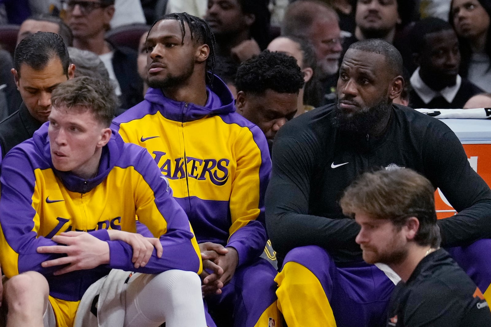 Los Angeles Lakers guard Bronny James, center, and forward LeBron James, right, watch from the bench with guard Dalton Knecht, left, in the first half of an NBA basketball game against the Cleveland Cavaliers, Wednesday, Oct. 30, 2024, in Cleveland. (AP Photo/Sue Ogrocki)