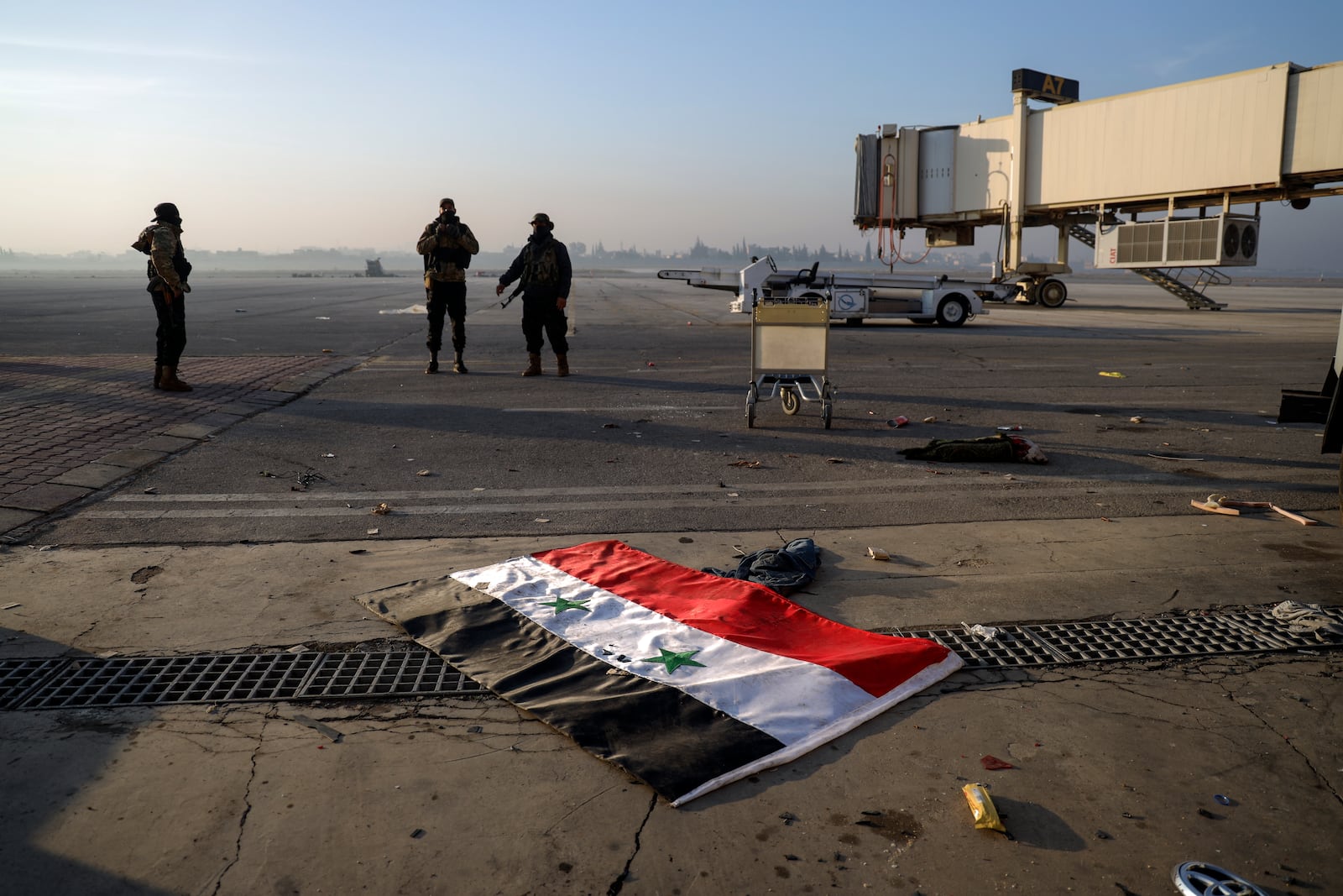 A Syrian official flag lies on the ground as opposition fighters stand on the tarmac of the Aleppo international airpot in Aleppo Monday, Dec. 2, 2024. .(AP Photo/Omar Albam)