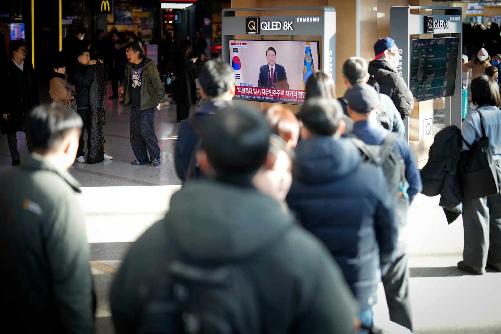 People watch a TV screen showing the live broadcast of South Korean President Yoon Suk Yeol's announcement at the Seoul Railway Station in Seoul, South Korea, Thursday, Dec. 12, 2024. (AP Photo/Lee Jin-man)