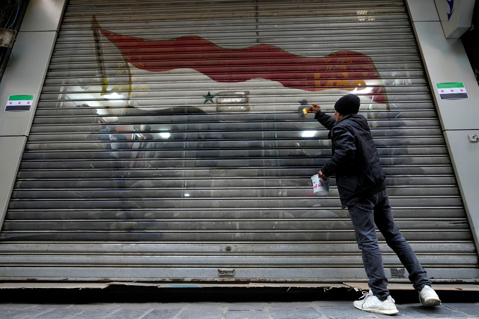 A worker removes from a door shop the colours of the official flag of the ousted government, in Damascus, Syria, Friday, Dec. 20, 2024. (AP Photo/Hussein Malla)