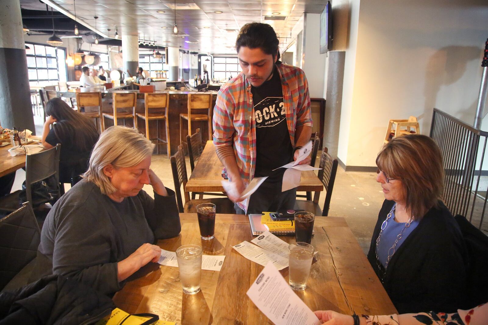 Louis Connelly, a bartender at Lock 27 Brewing in downtown Dayton, hands one-time use paper menus to guests Wednesday. The disposable menus are a response to the concerns about the coronavirus. The restaurant has also removed communal salt and pepper shakers and mustard and ketchup bottles from the tables and offers plastic cups and cutlery. LISA POWELL / STAFF