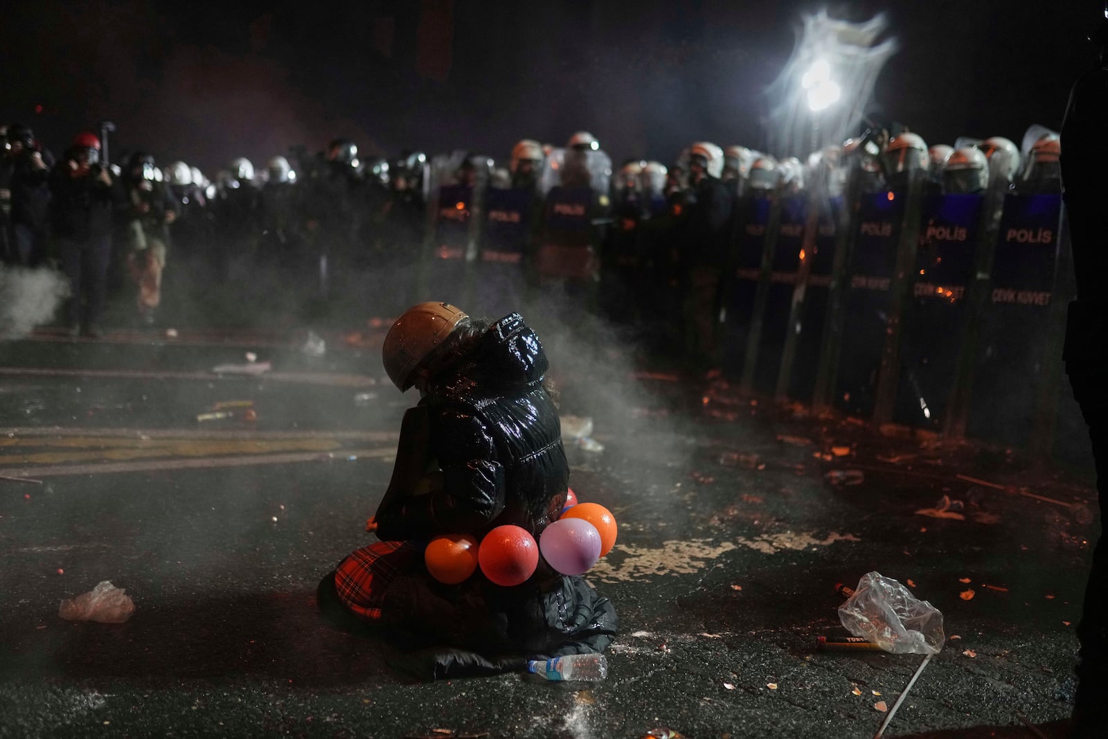 A protester sits on her knees as riot police stand guard during a protest against the arrest of Istanbul's Mayor Ekrem Imamoglu, in Istanbul, Turkey, Saturday, March 22, 2025. (AP Photo/Francisco Seco)