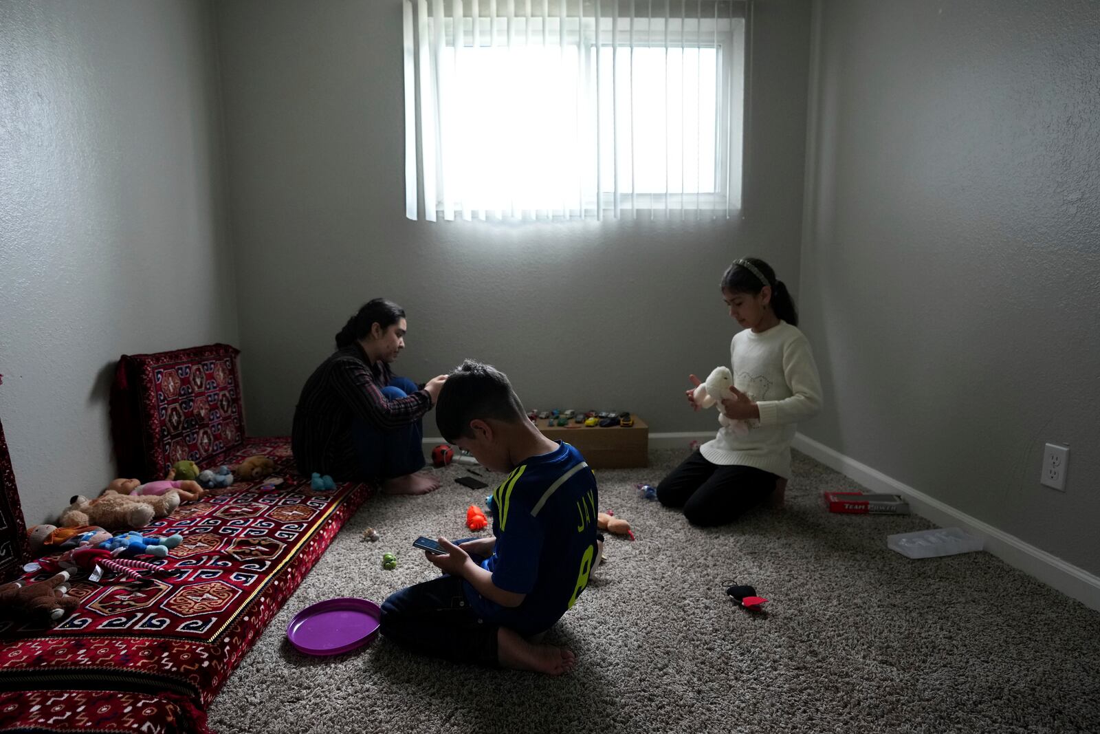 Afghans Nilaap Osmani, left, Mohammad Shabir Osmani, center and Nargis Osmani, right, spend some quiet time in their new home in Rancho Cordova, Calif., Wednesday, March 12, 2025. (AP Photo/Rich Pedroncelli)