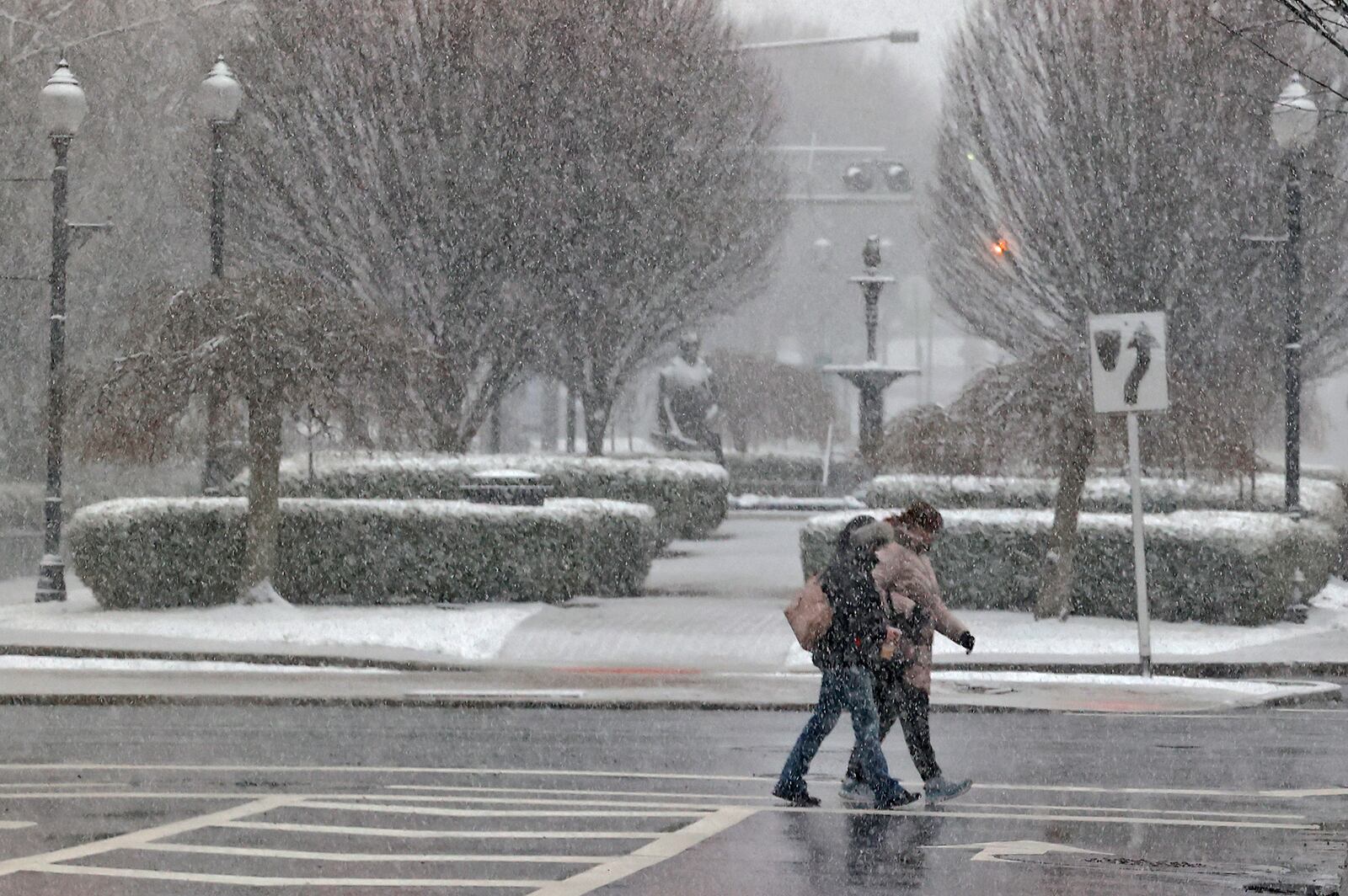 The snow Friday, Feb. 16, 2024 partially obscures two people as they cross Fountain Avenue in downtown Springfield. BILL LACKEY/STAFF