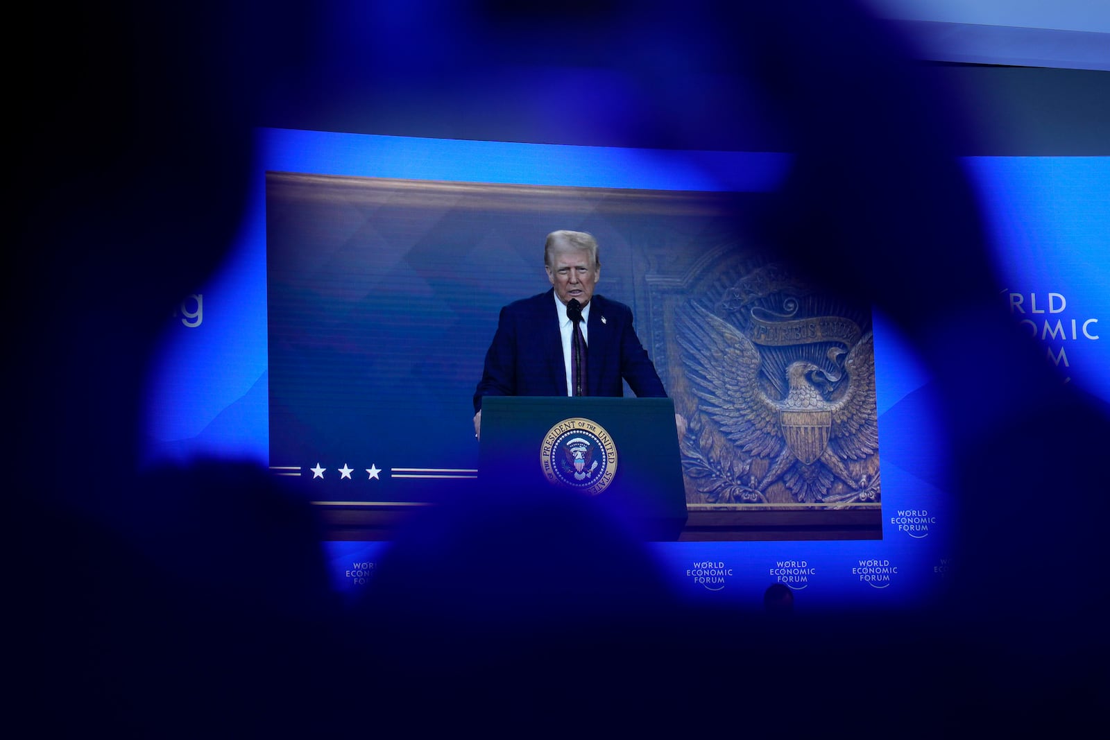 People follow a virtual speech of U.S. president Donald Trump at the Annual Meeting of World Economic Forum in Davos, Switzerland, Thursday, Jan. 23, 2025. (AP Photo/Markus Schreiber)