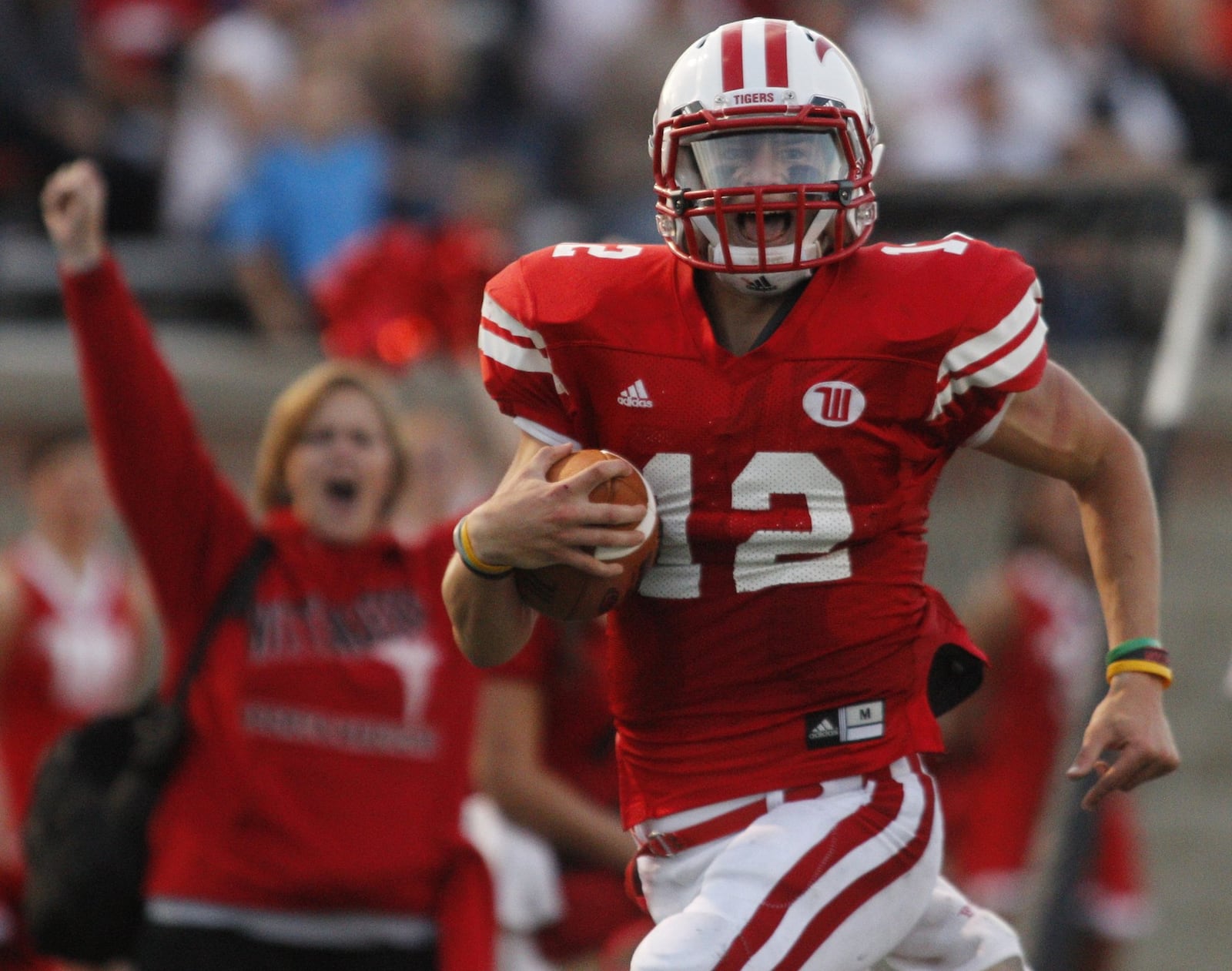 Wittenberg quarterback Reed Florence runs along the sideline en route to a touchdown against DePauw on Sept. 15 at Edwards-Maurer Field in Springfield, Ohio. Head trainer Ellen Crosbie cheers in the background. Barbara J. Perenic/Springfield News-Sun