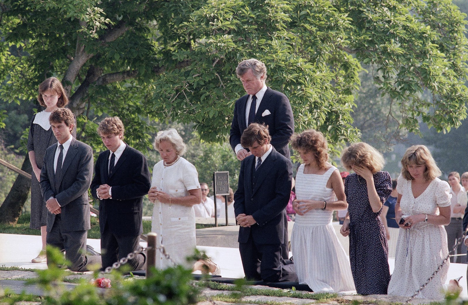 FILE - Members of the Kennedy family kneel at the grave site of the late President John F. Kennedy at Arlington National Cemetery after they visited the grave of the late Robert F. Kennedy nearby, on the anniversary of his death 16 years ago, June 6, 1984. From left: Emily and Robert F. Kennedy, Jr.; Chris Kennedy; Ethel Kennedy; Michael Kennedy and Kathleen Kennedy, the wife and children of Robert Kennedy. Sen. Edward M. Kennedy (D-Mass.) stands at back. (AP Photo/Barry Thumma, File)