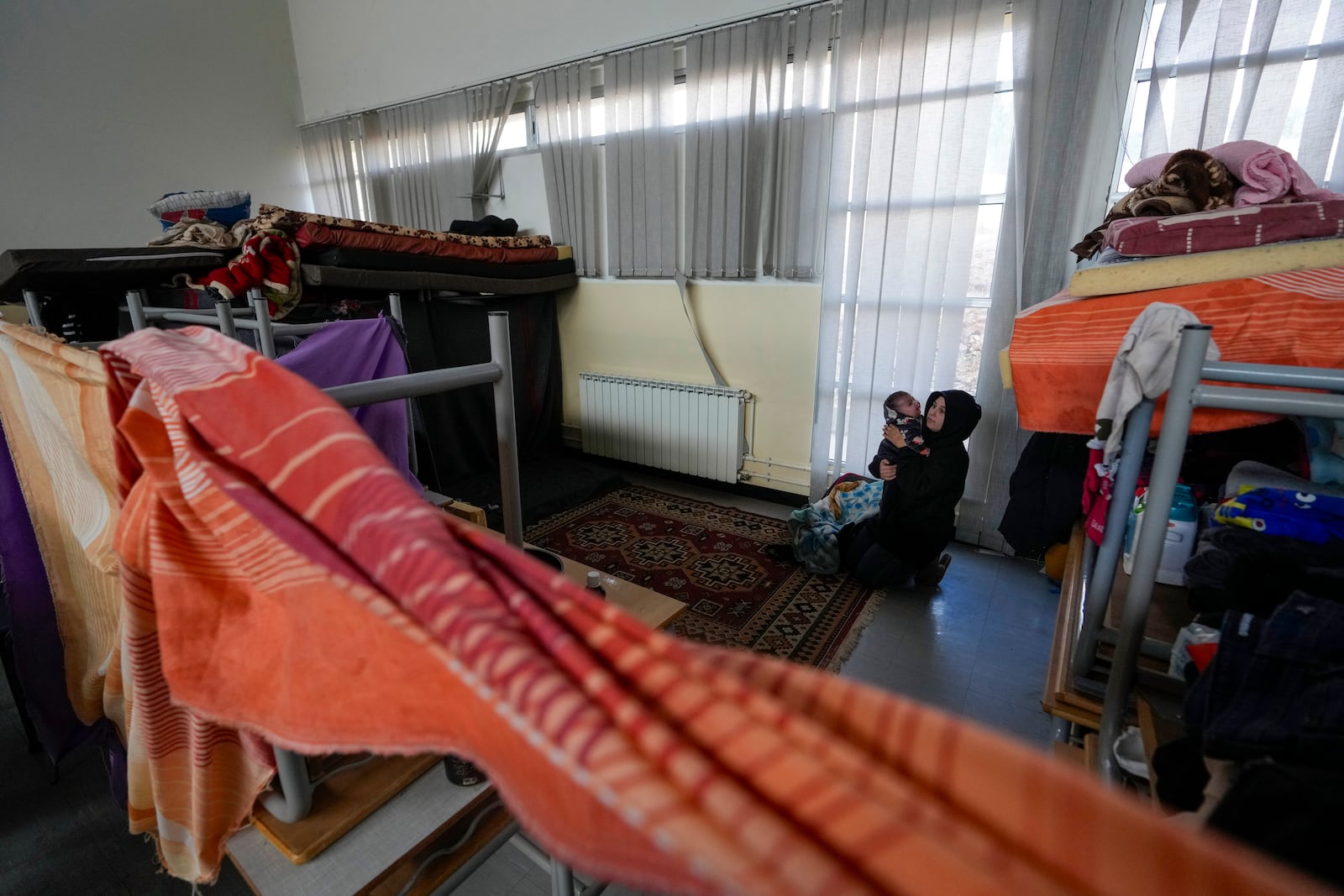 A displaced woman, who fled Baalbek city and the nearby towns of Douris and Ain Bourday amid the ongoing Hezbollah-Israel war, holds her daughter at a school being used as a shelter, in Deir Al-Ahmar, east Lebanon, Thursday, Oct. 31, 2024. (AP Photo/Hassan Ammar)