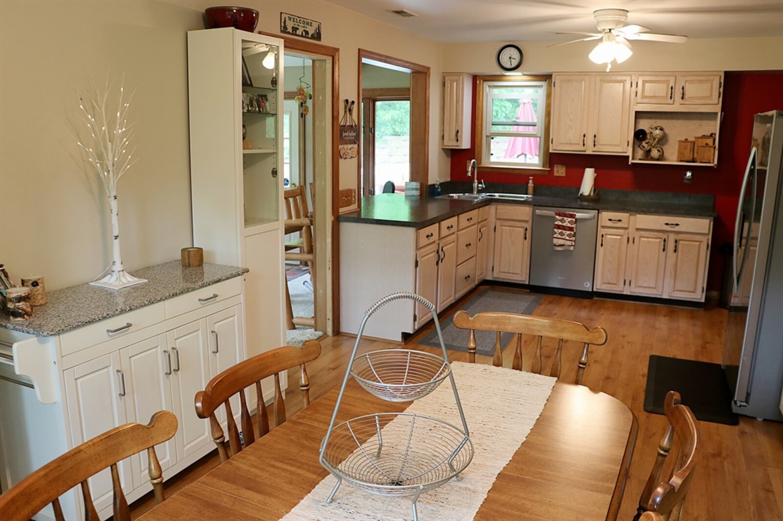 The L-shaped kitchen has been updated with light cabinetry and dark countertops. A double-door pantry cabinet is near the dining area. A double sink is tucked into one corner and a small window is above the sink. A pass-through cutout has an extended countertop that creates a two-seat bar within the four-season family room. Contributed photo 