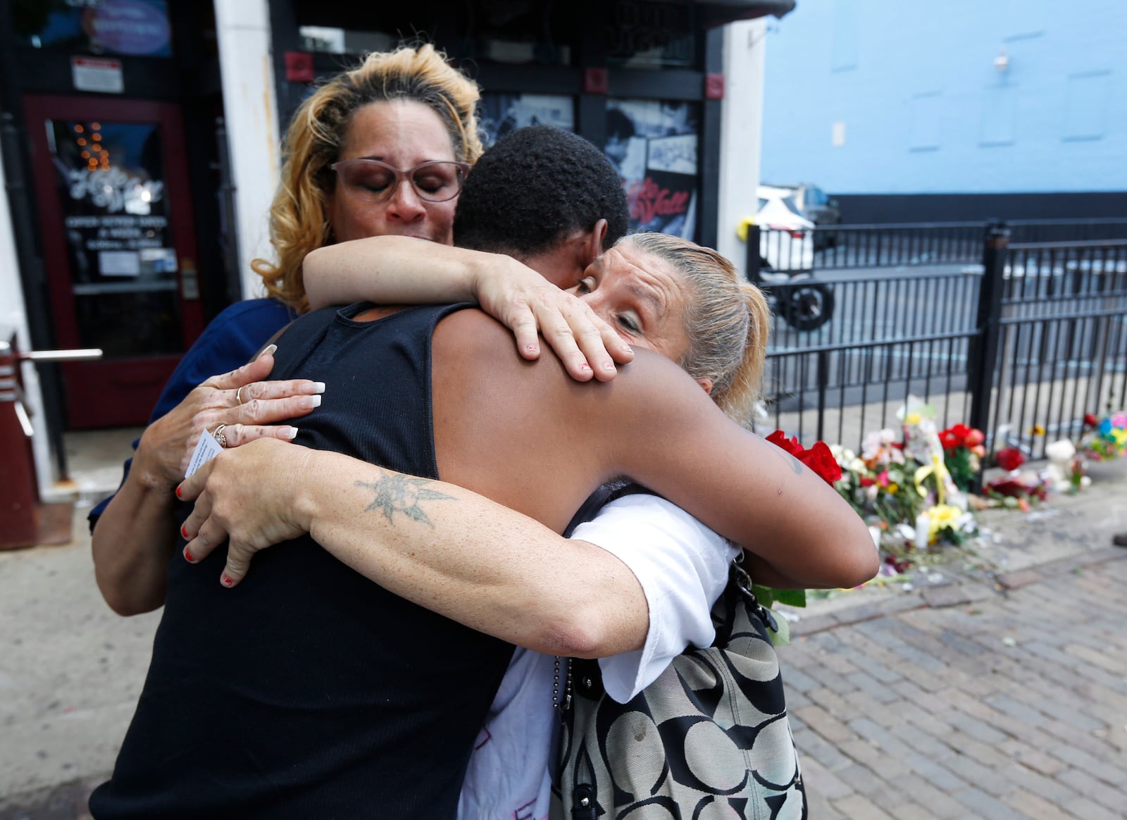 Harry Payne is hugged by Jean Davies, left, and Mary K. Curtis as he arrived on East Fifth Street on Monday to leave flower for his slain friend Logan Turner who was gunned down early Sunday morning with eight other victims.  TY GREENLEES / STAFF