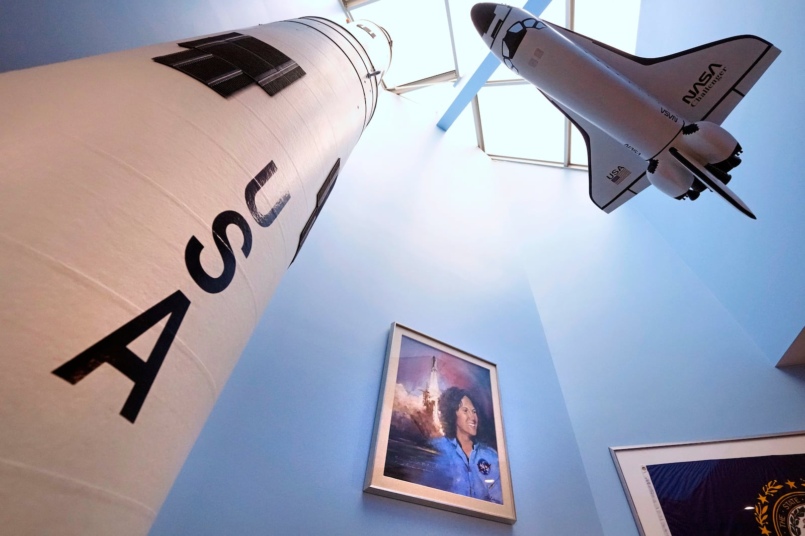 A model of the space shuttle Challenger, at right, floats above a portrait of NASA's first teacher in space Christa McAuliffe at the McAuliffe-Shepard Discovery Center, Monday, Dec. 16, 2024, in Concord, N.H. (AP Photo/Charles Krupa)