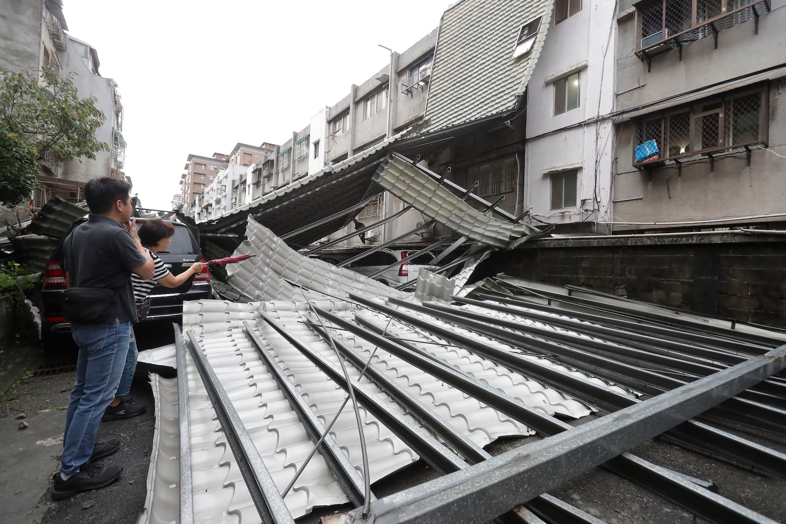 Two car owners look at their car smashed by a row of blown roofs due to the wind of Typhoon Kong-rey in Taipei, Taiwan, Friday, Nov. 1, 2024. (AP Photo/Chiang Ying-ying)