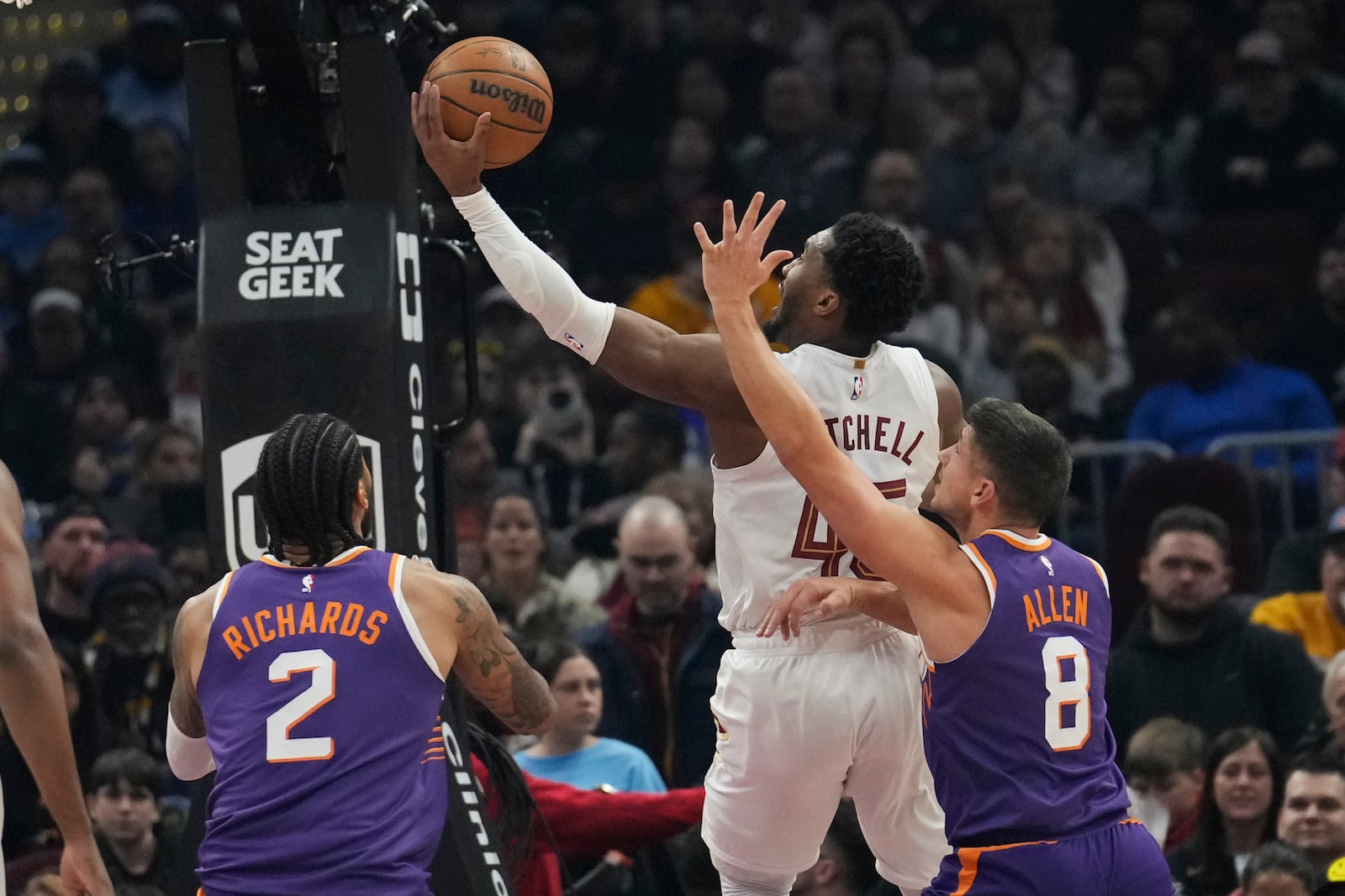 Cleveland Cavaliers guard Donovan Mitchell, second from right, goes to the basket between Phoenix Suns center Nick Richards (2) and guard Grayson Allen (8) in the first half of an NBA basketball game, Monday, Jan. 20, 2025, in Cleveland. (AP Photo/Sue Ogrocki)