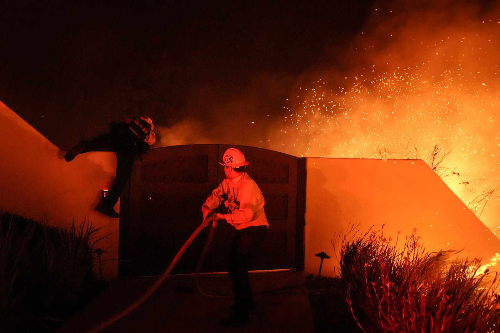 Embers fly in gusty winds as two Los Angeles County firefighters battle the Franklin Fire at Pepperdine University in Malibu, Calif., Tuesday, Dec. 10, 2024. (AP Photo/Jae C. Hong)