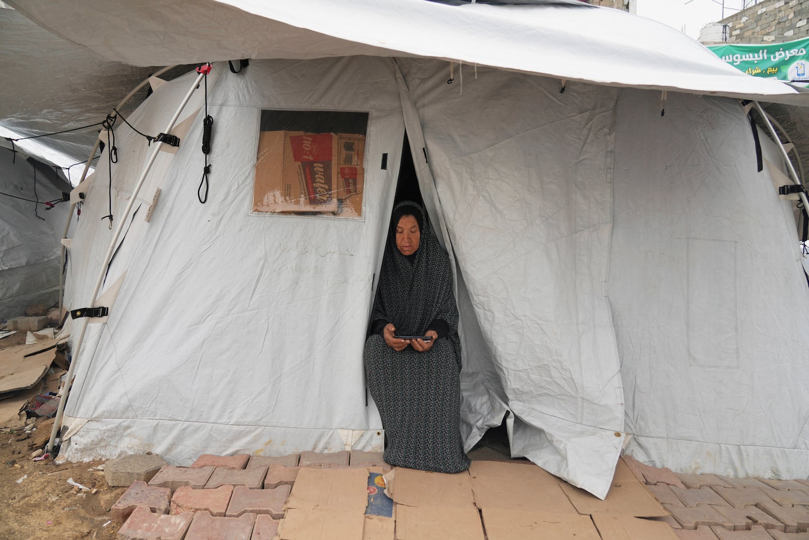 A displaced Palestinian woman sits in the doorway to her tent in a sprawling camp adjacent to destroyed homes and buildings in Gaza City, Gaza Strip, Saturday, March 1, 2025 during the Muslim holy month of Ramadan. (AP Photo/Abdel Kareem Hana)