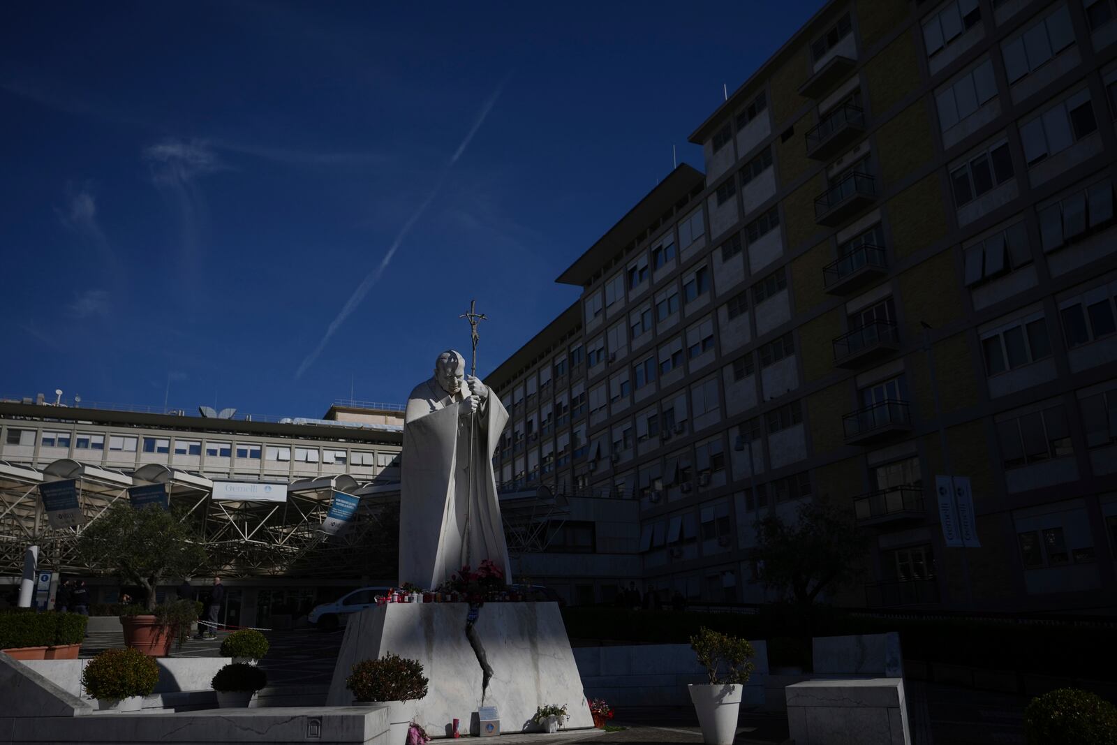 A marble statue of late Pope John Paul II is engulfed by the shade cast by the Agostino Gemelli Polyclinic in Rome, Sunday, Feb. 16, 2025, where Pope Francis was hospitalised Friday after a week-long bout of bronchitis worsened and is receiving drug therapy for a respiratory tract infection that made impossible for him to attend the traditional Sunday public blessing after the noon Angelus prayer. (AP Photo/Alessandra Tarantino)