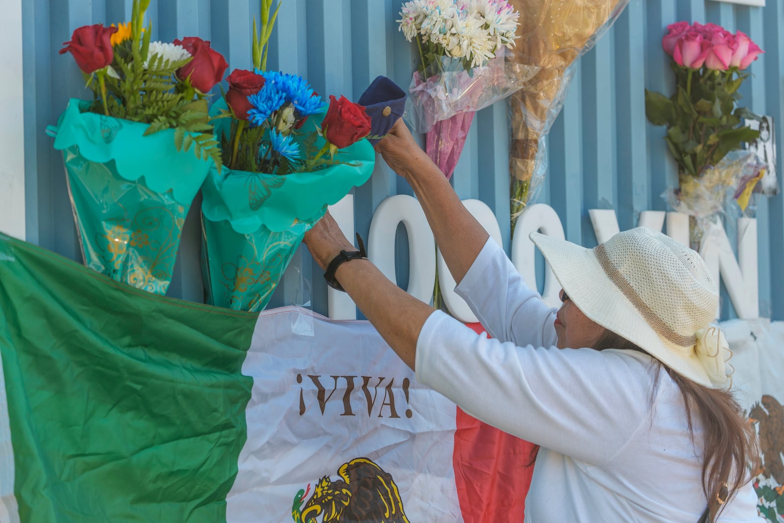 Cristina Vargas from North Hollywood, places a Mexican flag among baseball memorabilia, flowers, and candles placed outside Dodger Stadium after the death of former Dodgers pitcher Fernando Valenzuela Wednesday, Oct. 23, 2024, in Los Angeles. Valenzuela, the Mexican-born phenom for the Los Angeles Dodgers who inspired "Fernandomania" while winning the NL Cy Young Award and Rookie of the Year in 1981, died Tuesday, Oct. 22, 2024. (AP Photo/Damian Dovarganes)