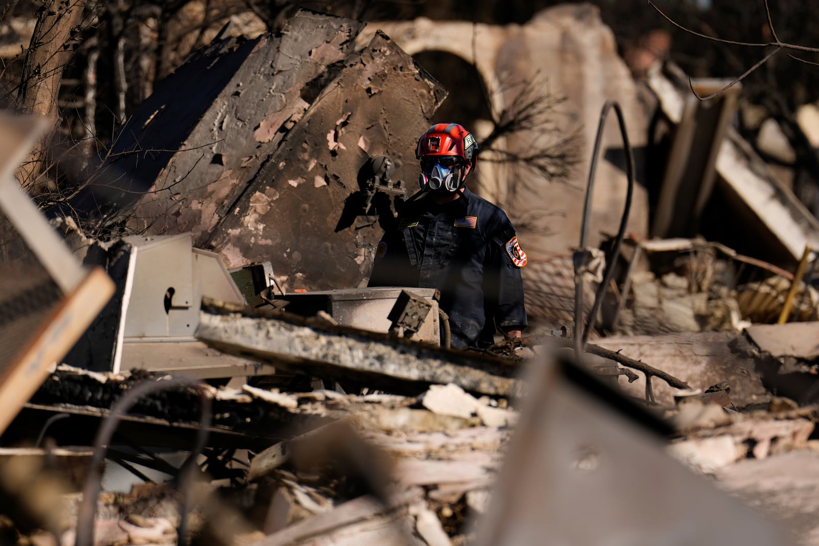 A member of a San Bernardino County Fire Department Search and Rescue crew works among the ruins of the Palisades Fire in the Pacific Palisades neighborhood of Los Angeles, Tuesday, Jan. 14, 2025. (AP Photo/Carolyn Kaster)