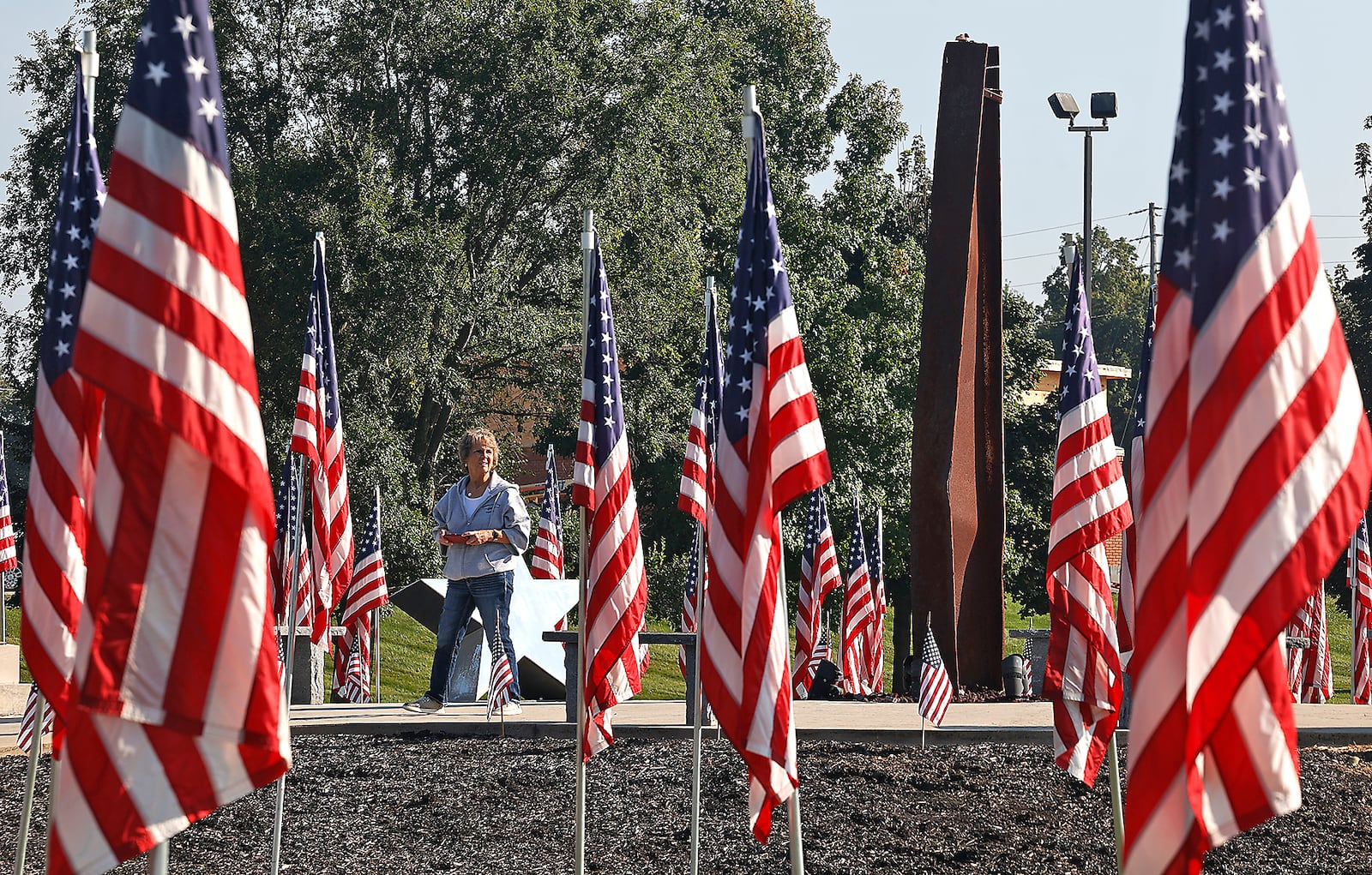 Sally McInturff Powers looks at the sea of American flags surrounding the World Trade Center artifact Monday, Sept. 11, 2023 at Freedom Grove in Urbana. BILL LACKEY/STAFF