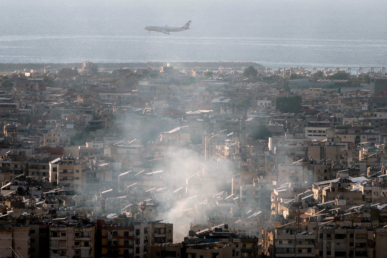 A Middle East Airlines airplane flies over Dahiyeh as smoke rises from Israeli an airstrike, in the southern suburb of Beirut, Lebanon, Saturday, Nov. 16, 2024. (AP Photo/Bilal Hussein)