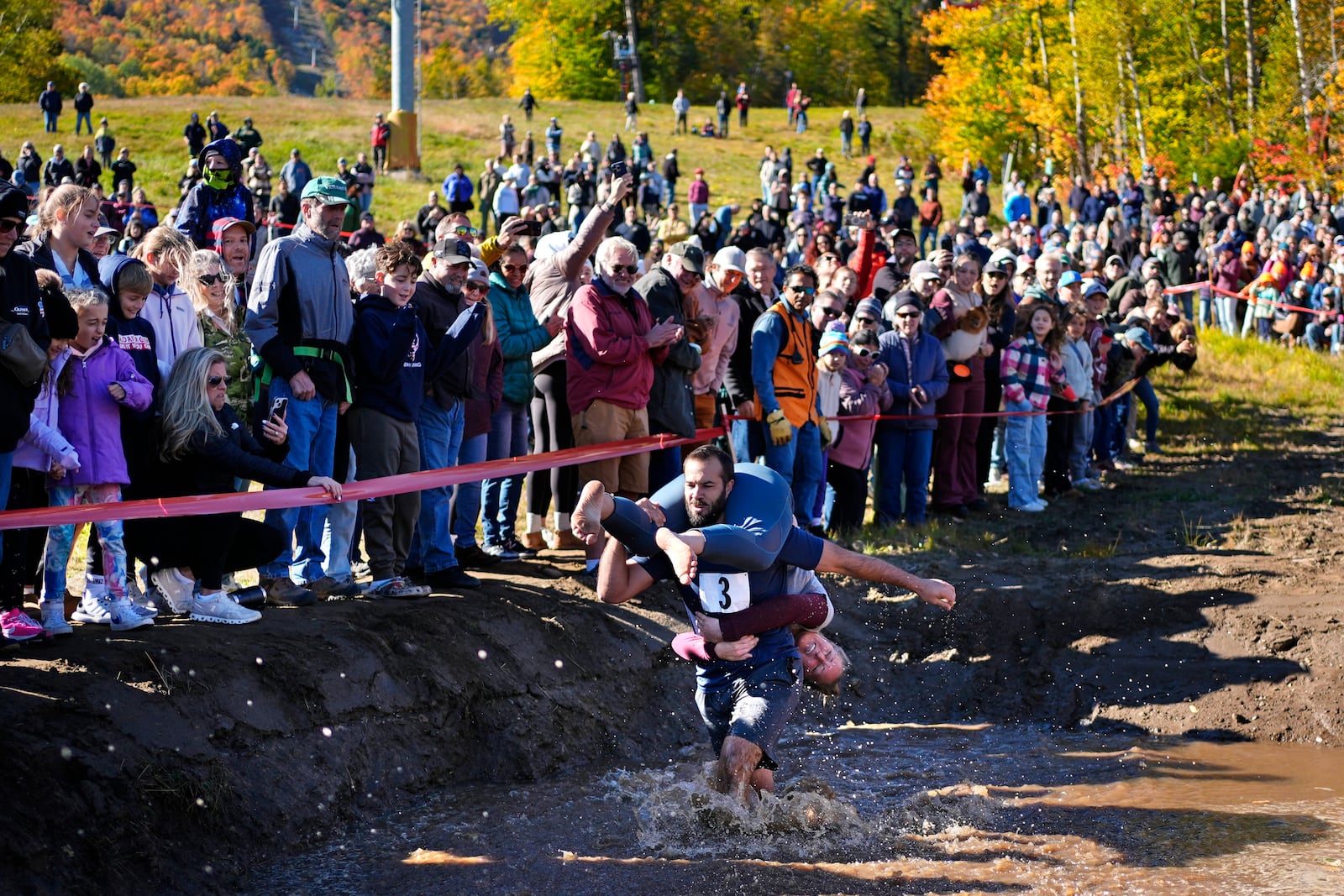 Jon Heaner splashes through the water hazard while carrying Renee Heaner during the North American Wife Carrying Championship, Saturday, Oct. 12, 2024, at Sunday River ski resort in Newry, Maine. (AP Photo/Robert F. Bukaty)